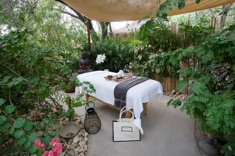 Outdoor massage bed nestled in lush garden with white linens and tropical plants overhead