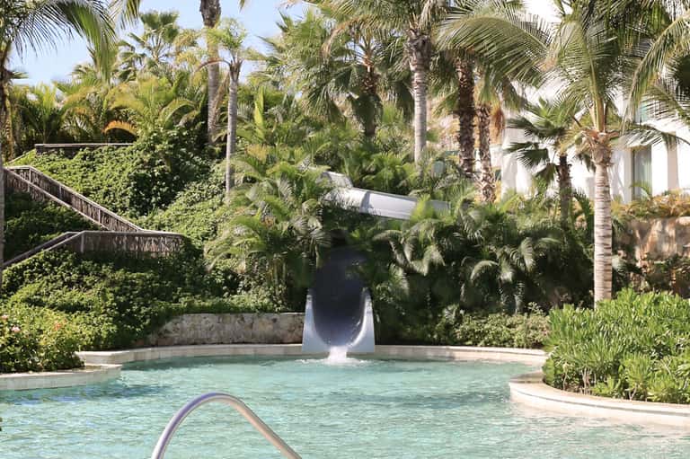 Resort water slide cascading into tropical pool surrounded by palm trees and lush vegetation