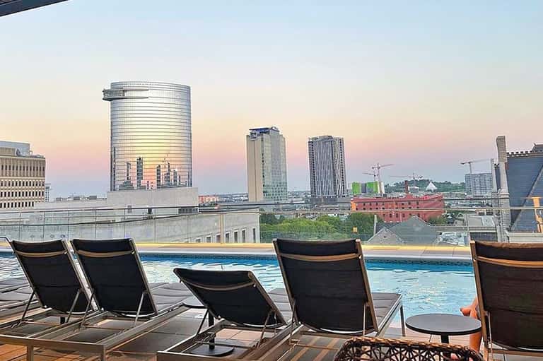 Rooftop pool deck with lounge chairs and city skyline at dusk