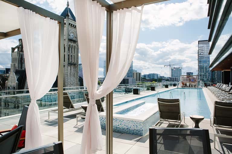 Elegant rooftop pool with sheer curtains, lounge chairs, and city skyline view with historic clock tower