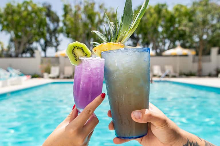 Two colorful tropical cocktails by the pool with fruit garnishes
