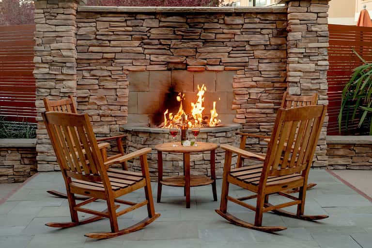 Outdoor fireplace with stone surround and wooden rocking chairs on patio seating area