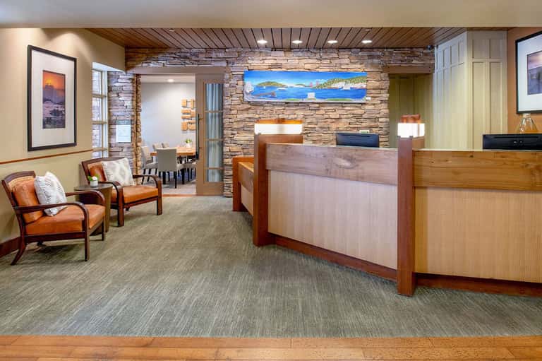 Hotel lobby interior with stone fireplace accent wall, wooden reception desk, leather seating, and coastal artwork