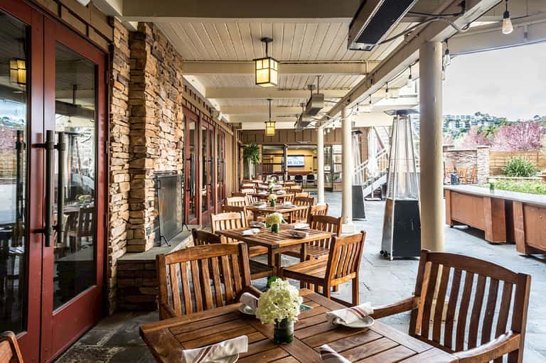 Covered patio dining area with wooden tables, brick fireplace, and garden views