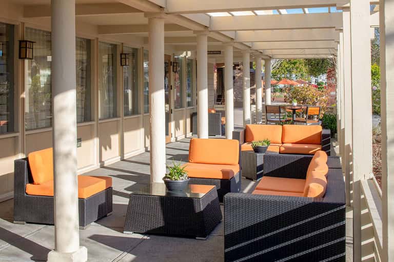 Covered outdoor patio with orange cushioned seating, black wicker furniture, and glass doors