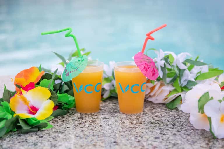 Two tropical juice drinks with colorful umbrellas and straws surrounded by vibrant flowers