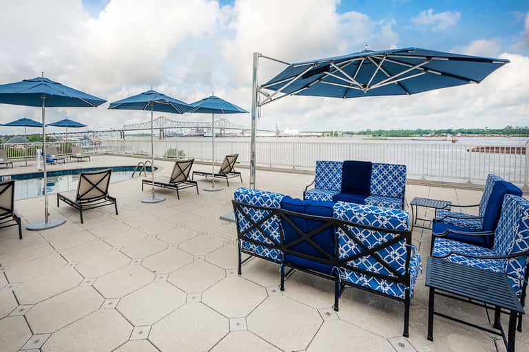 Waterfront patio with blue umbrellas, patterned seating, and river bridge view