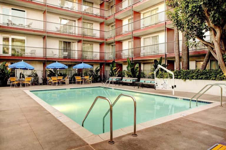 Hotel courtyard with swimming pool, blue umbrellas, yellow chairs, and red-brick building facade