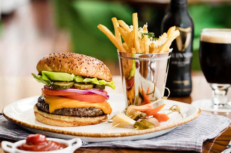 Gourmet burger with fries and dark beer on wooden table with pickles and garnish