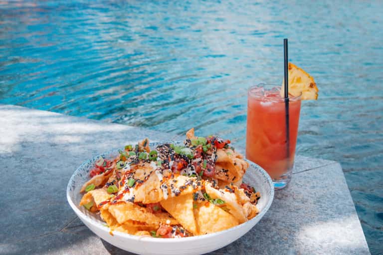 Spicy appetizer bowl served poolside with tropical cocktail and ocean view backdrop