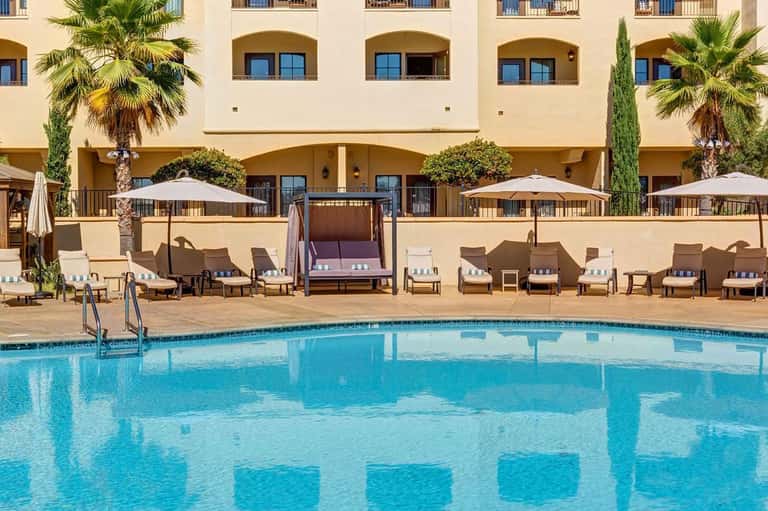 Resort pool with lounge chairs, umbrellas, and Mediterranean-style building facade