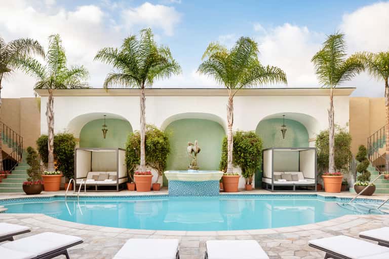 Resort pool with turquoise water, palm trees, arched alcoves, lounge chairs, and terracotta pots