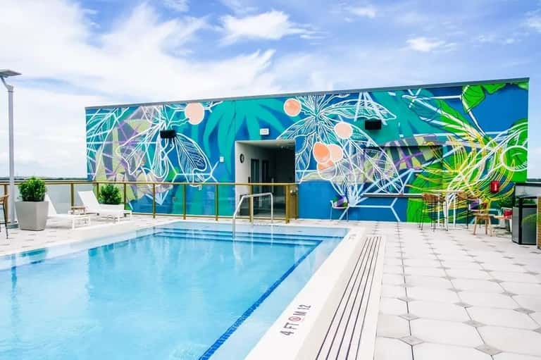 Modern rooftop pool with turquoise water, botanical mural backdrop, and white patio seating