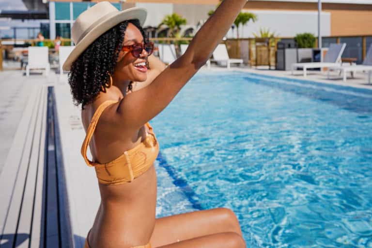 Woman in yellow bikini at pool edge wearing hat and sunglasses, enjoying resort amenities