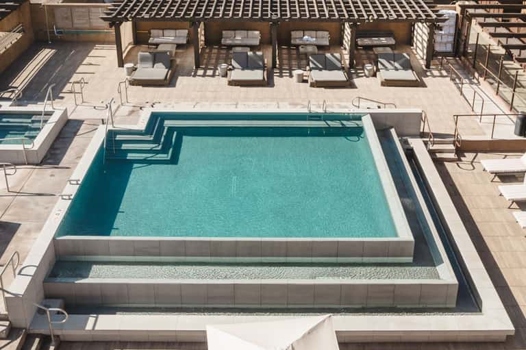 Aerial view of multi-level pool deck with lounge chairs, umbrellas, and modern architectural design