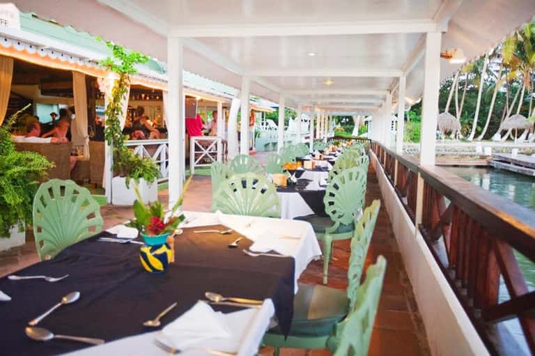 Waterfront dining area with turquoise shell-back chairs and tropical plants