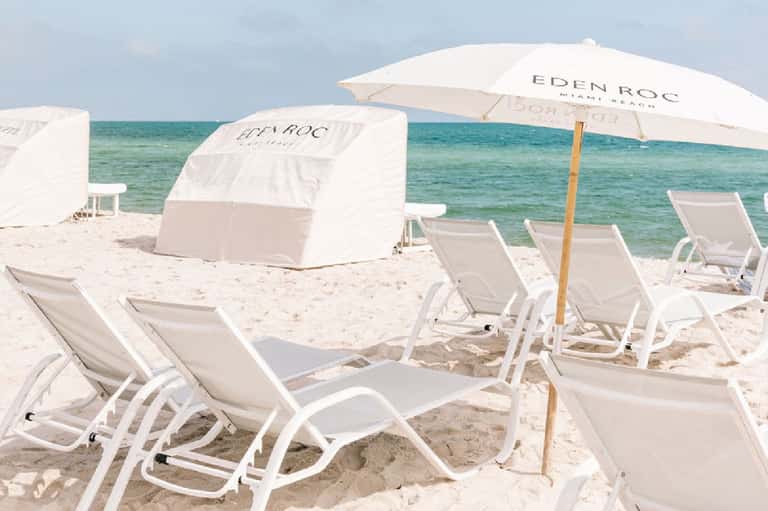 Sandy beach with white lounge chairs, umbrellas, and turquoise ocean water