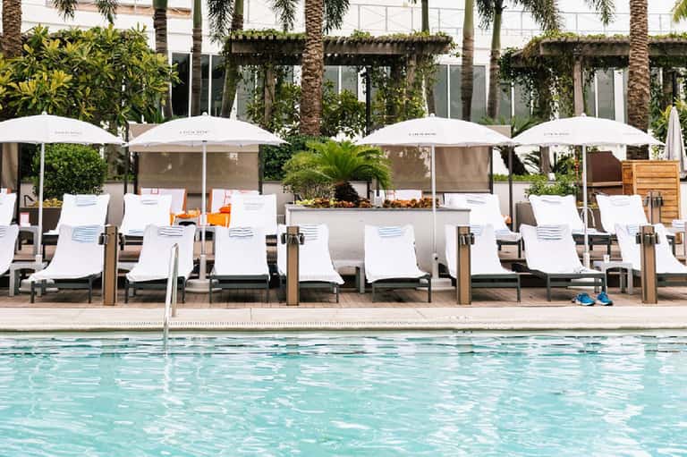 Resort poolside lounge area with white umbrellas, sun loungers, and modern architecture
