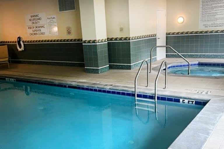 Indoor swimming pool with turquoise water, tiled walls, and metal railings