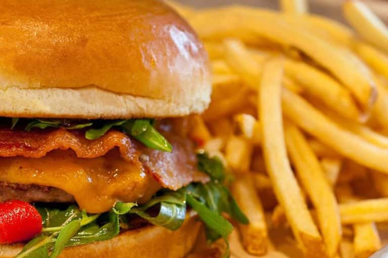 Close-up of gourmet burger with crispy bacon, cheese, greens, and golden French fries
