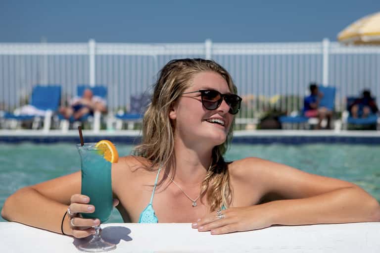 Woman in turquoise bikini enjoying a blue cocktail while relaxing in a resort pool