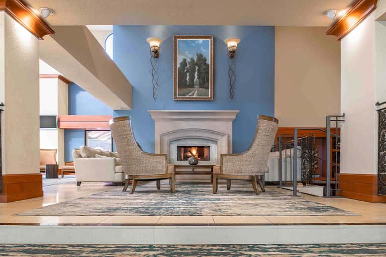 Elegant fireplace lounge with blue accent wall, upholstered chairs, decorative sconces, and wooden trim
