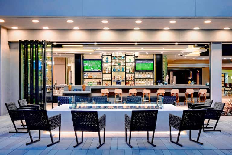 Modern outdoor bar counter with black woven chairs and open-air design at resort