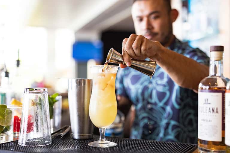 Bartender pouring cocktail into glass with citrus fruit and ice at resort bar