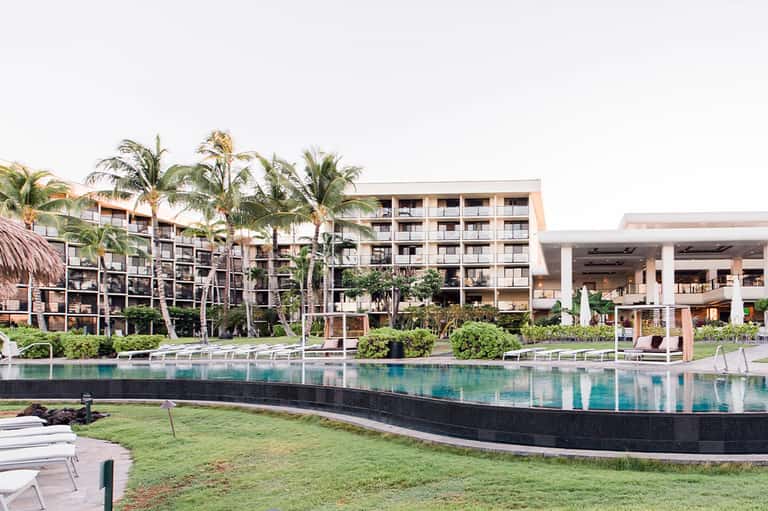Modern resort property featuring sleek lap pool, contemporary architecture, palm trees, lounge areas, and multi-story hotel buildings