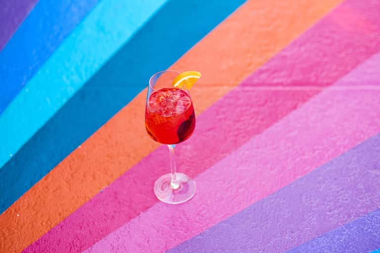 Vibrant red cocktail with lemon garnish on colorful striped background