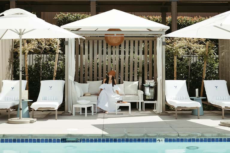 Woman in white dress sitting in cabana with white umbrellas by pool