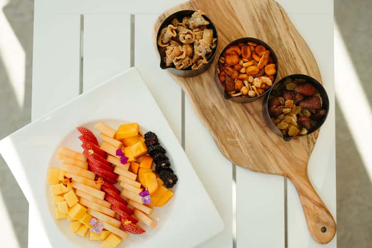 Fruit and snack board with colorful arranged cheese, strawberries, and various nuts in bowls