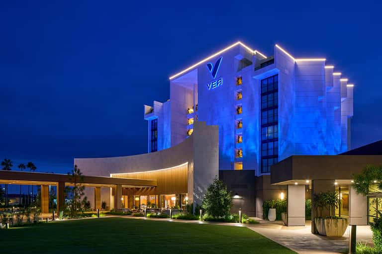 Modern hotel building illuminated in blue at dusk with neon outline trim and palm trees