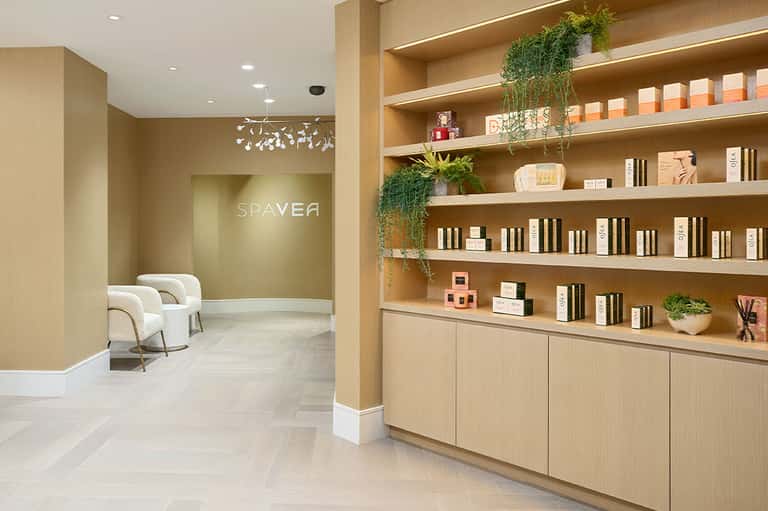 Spa entrance with light wood shelving displaying wellness products and modern white furnishings
