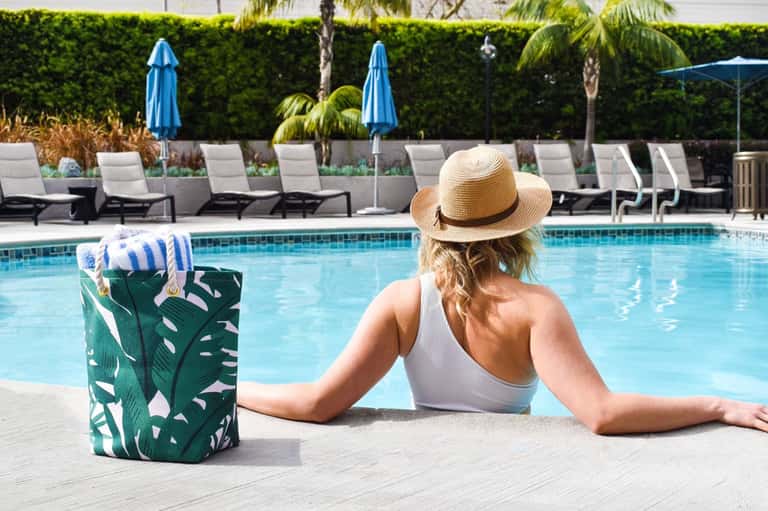 Woman relaxing in pool wearing sun hat with lounge chairs and umbrellas in background