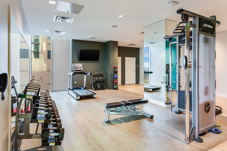 Modern fitness center with dumbbells, treadmill, exercise machines, and flat-screen TV
