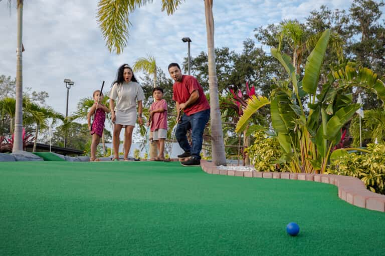 Family playing mini golf on tropical resort course with palm trees