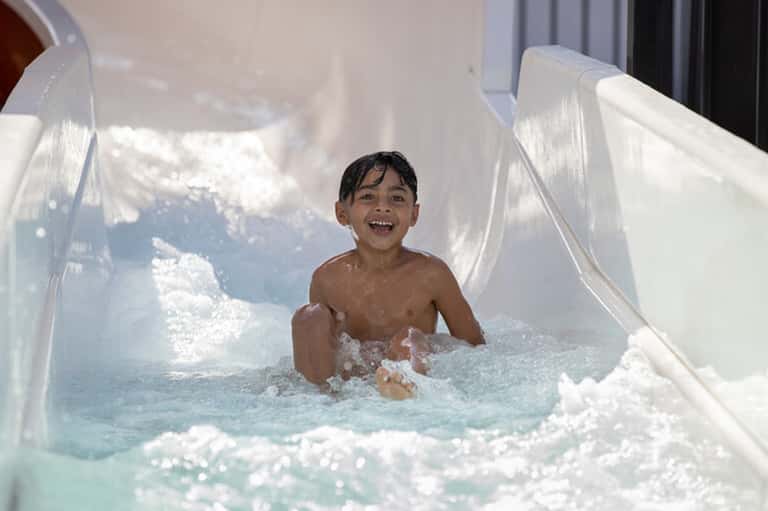 Young child sliding down white water slide into turquoise pool with splashing water
