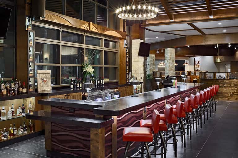 Upscale bar with long counter, red leather stools, wood accents, and pendant lighting
