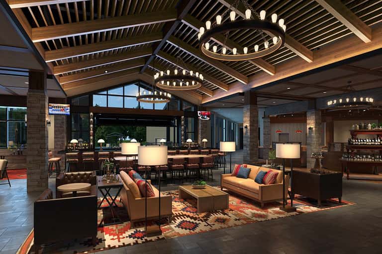 Upscale hotel lobby with wooden ceiling beams, circular chandeliers, tan sofas, and contemporary furnishings