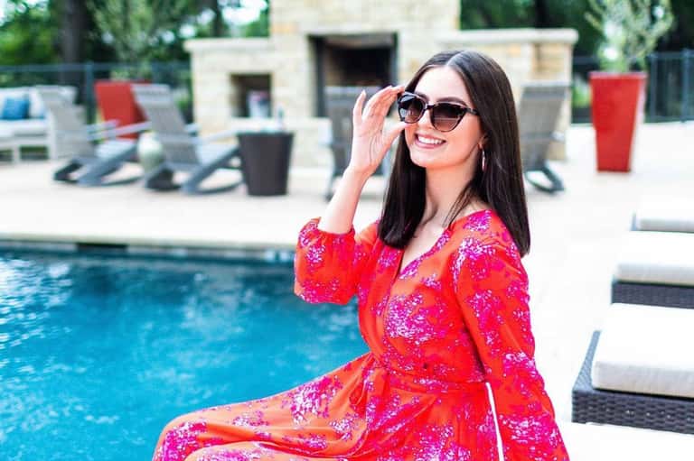Woman in colorful dress by poolside with lounge chairs and white building