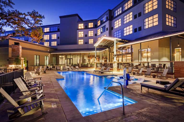 Illuminated resort pool at night surrounded by modern building architecture and lounge chairs