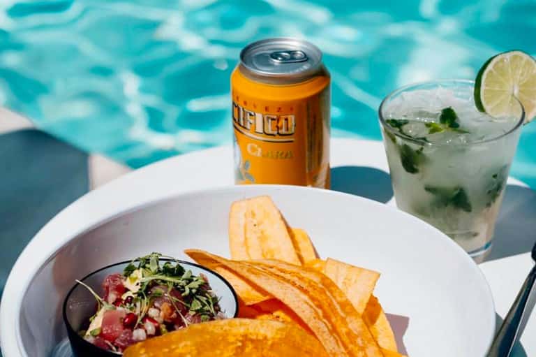 Poolside dining with ceviche dish, orange soda, and mojito cocktail against turquoise water backdrop