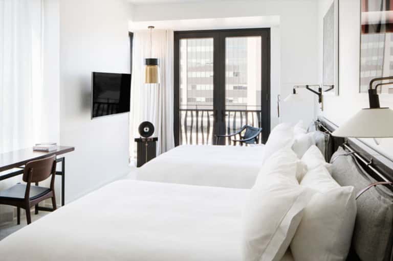 Contemporary hotel room with two beds, flat-screen TV, balcony doors, and city views