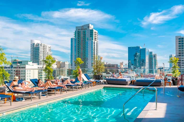 Rooftop pool with lounge chairs overlooking a city skyline with modern buildings and blue sky