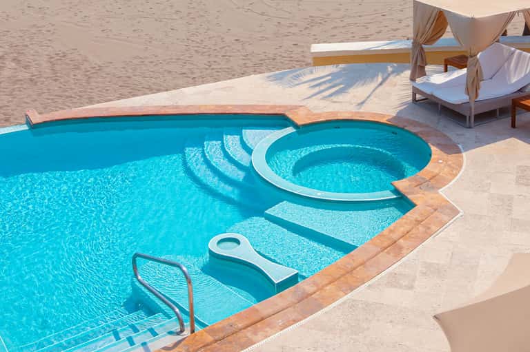 Luxury beachfront pool with spa hot tub, cabanas with white drapes, and sandy beach access