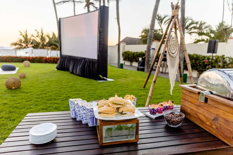 Outdoor lawn setup with food table, outdoor movie screen, and boho décor for evening event