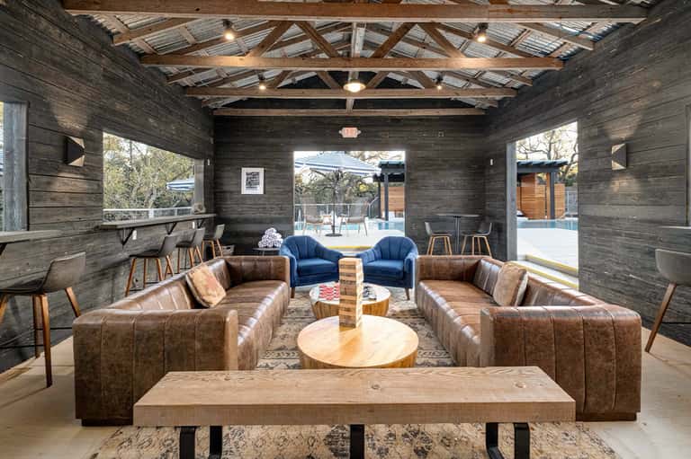 Modern lounge area with leather couches, wooden beams, blue accent chairs, and open patio