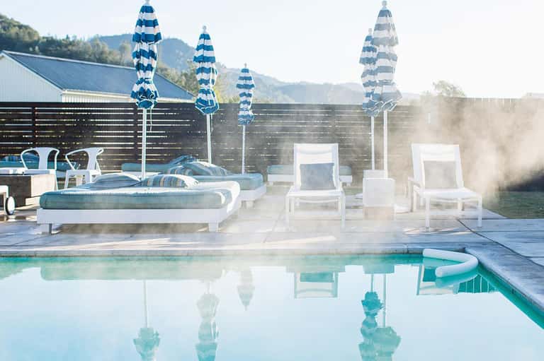 Modern pool with white loungers, blue striped umbrellas, and mountain views