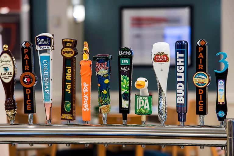 Beer tap handles displaying various brewery brands and styles at an indoor bar counter